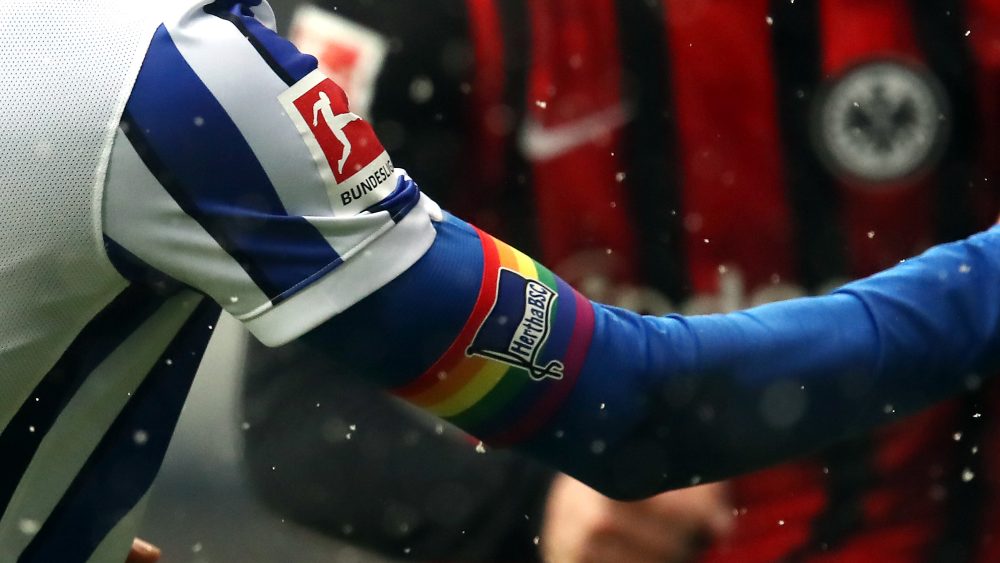 Ein Arm eines Hertha-Spielers mit einer Kapitänsbinde in Regenbogenfarben.