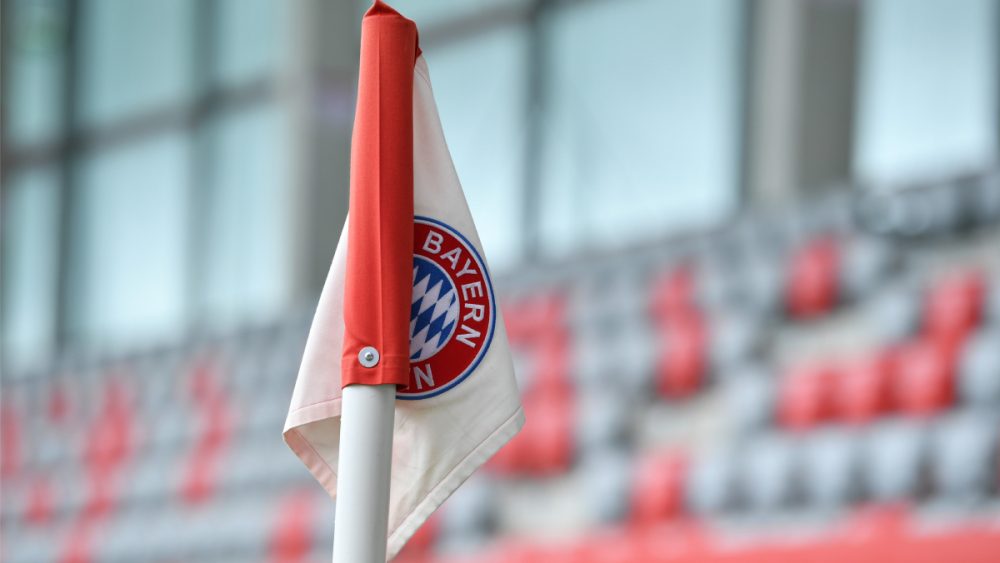 Eine Eckfahne, vor einer Tribüne am FC Bayern Campus. Auf der Fahne ist das Bayern-Logo zu sehen.