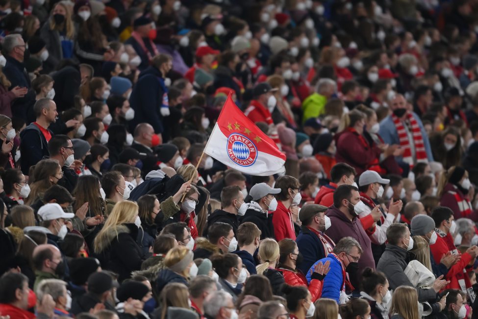 Fans des FC Bayern. In der Mitte eine rot-weiße Fahne mit FCB-Logo.