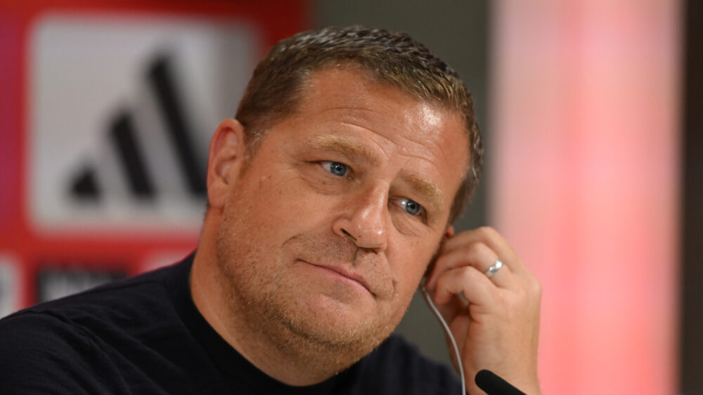 Max Eberl vom FC Bayern München sitzt auf dem Podium der Pressekonferenz und hält sich das linke Ohr.