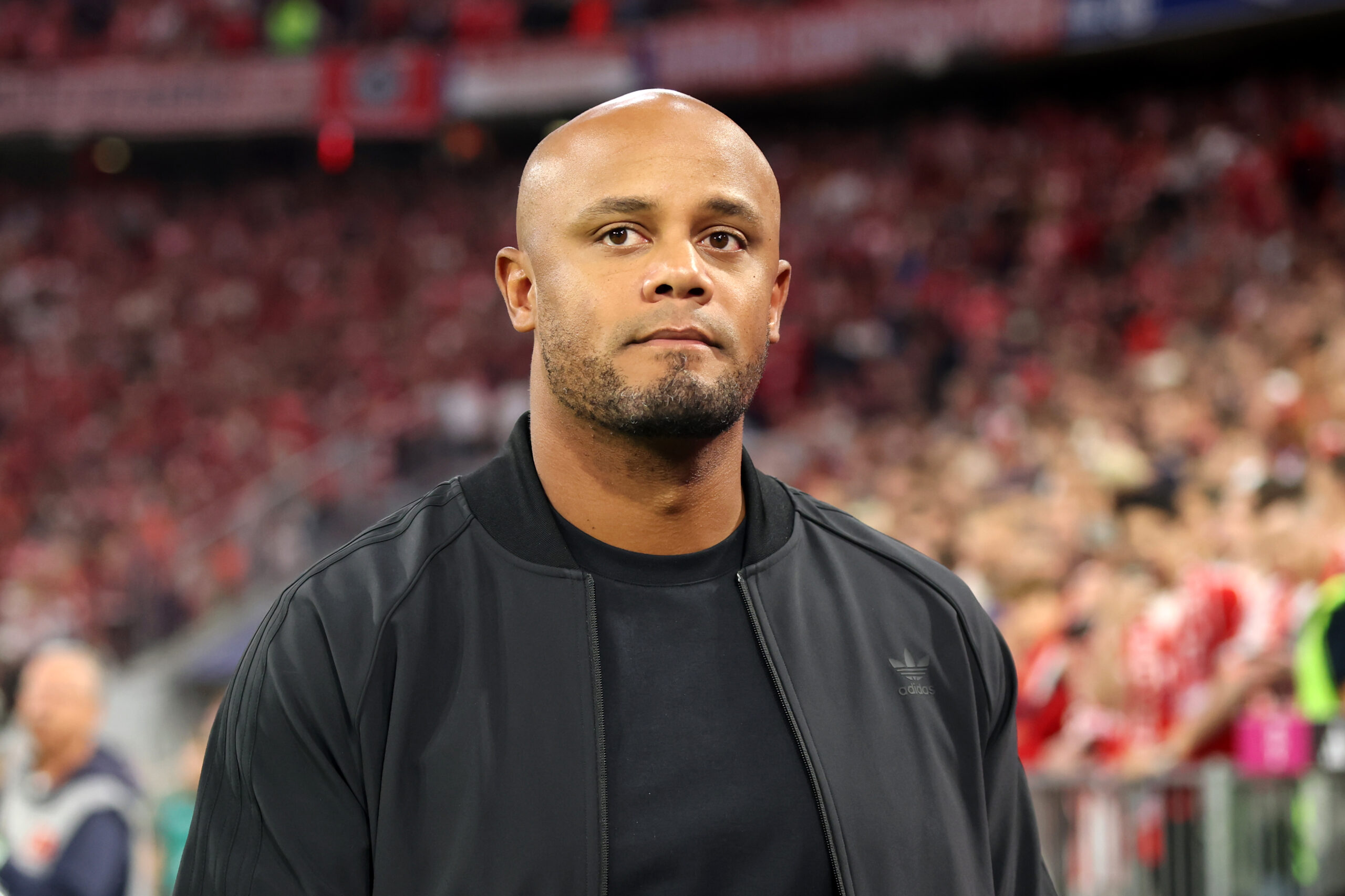 Vincent Kompany vom FC Bayern in dunkler Kleidung, hinter ihm das Publikum in der Allianz Arena.