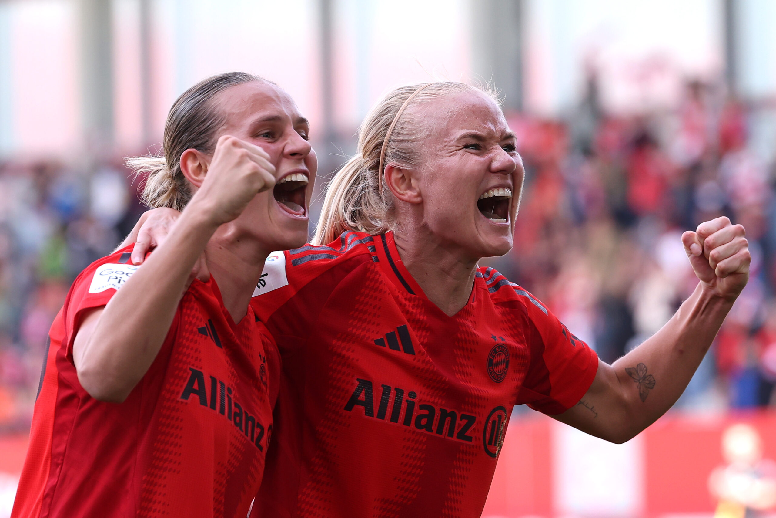 Klara Bühl und Pernille Harder freuen sich über ein Tor. Sie schreien mit freudigen Gesichtern in Richtung Fans und ballen die Fäuste. Sie tragen dabei das rote Heimtrikot der FC Bayern Frauen.