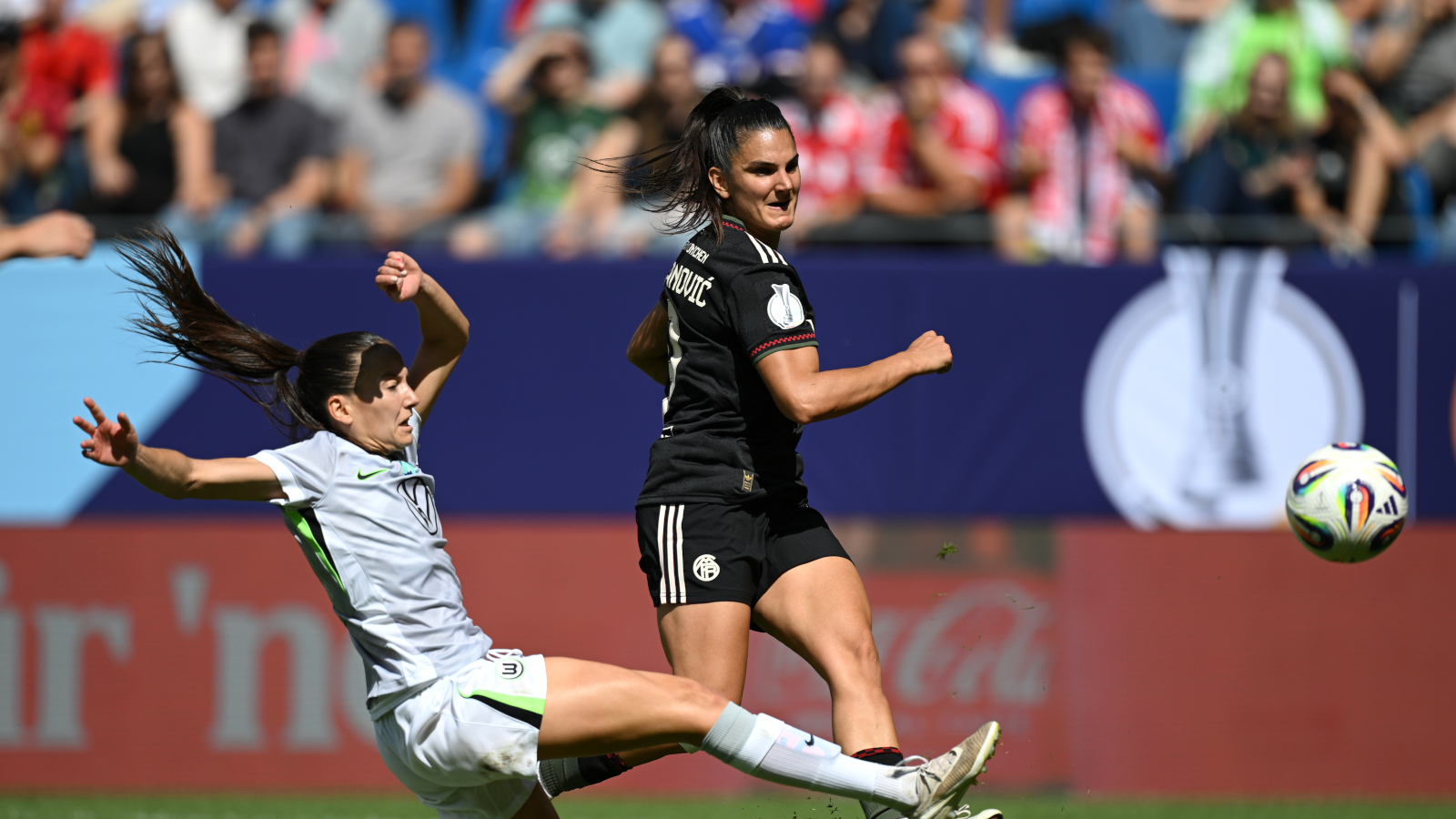 Jovana Damnjanovic (FC Bayern Frauen) schießt den Ball in Richtung Tor. Ihre Gegenspielerin vom VfL Wolfsburg kommt zu spät mit einer Grätsche.