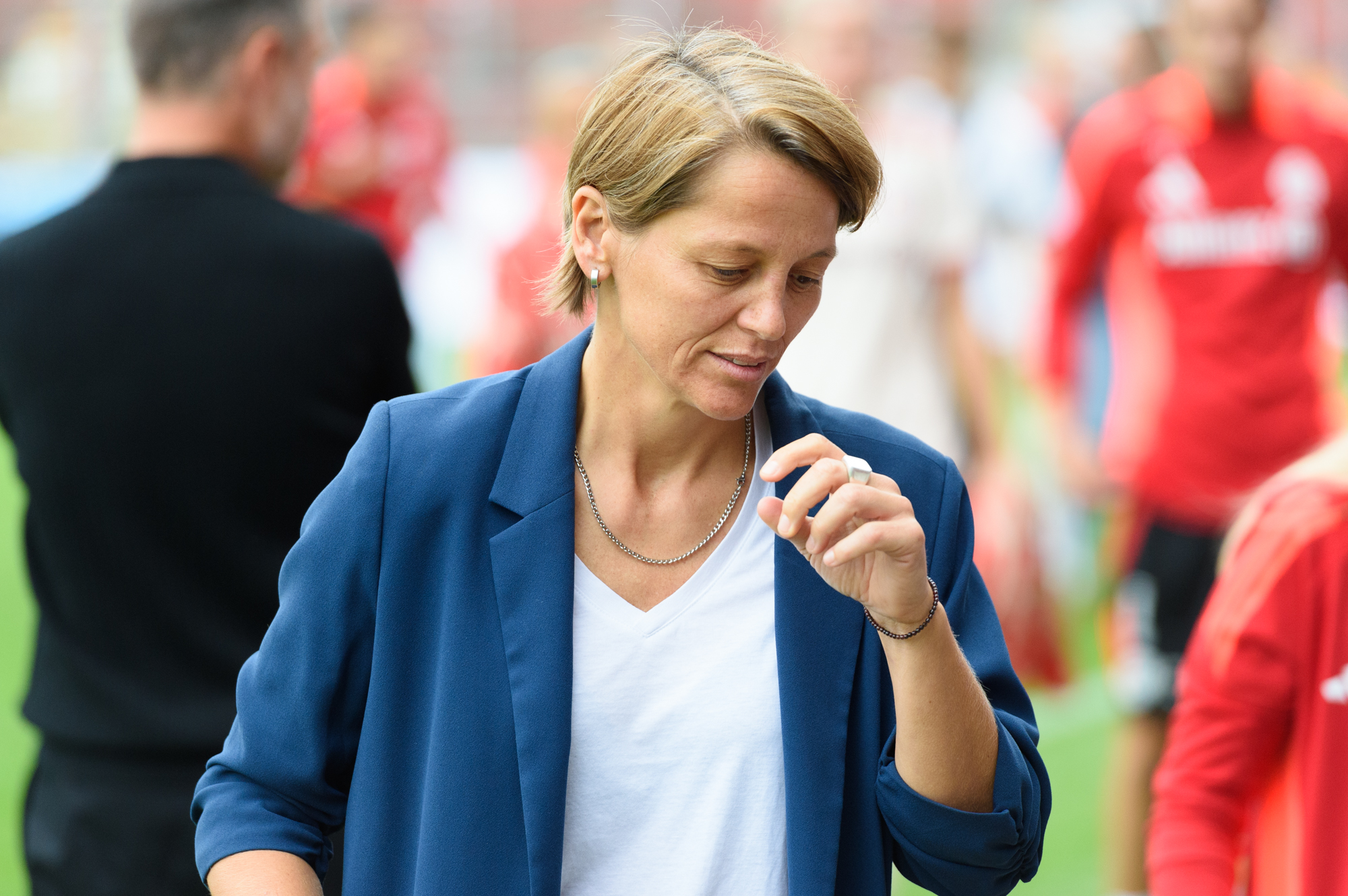 Bianca Rech schaut nach unten und hebt den linken Arm etwas. Im Hintergrund ist Personal der FC Bayern Frauen zu sehen.