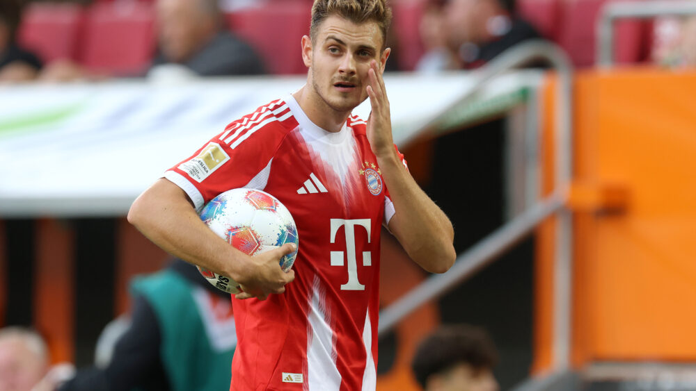 Josip Stanisic fässt sich ins Gesicht. Er hat einen Ball in der Hand und trägt das Trikot des FC Bayern.