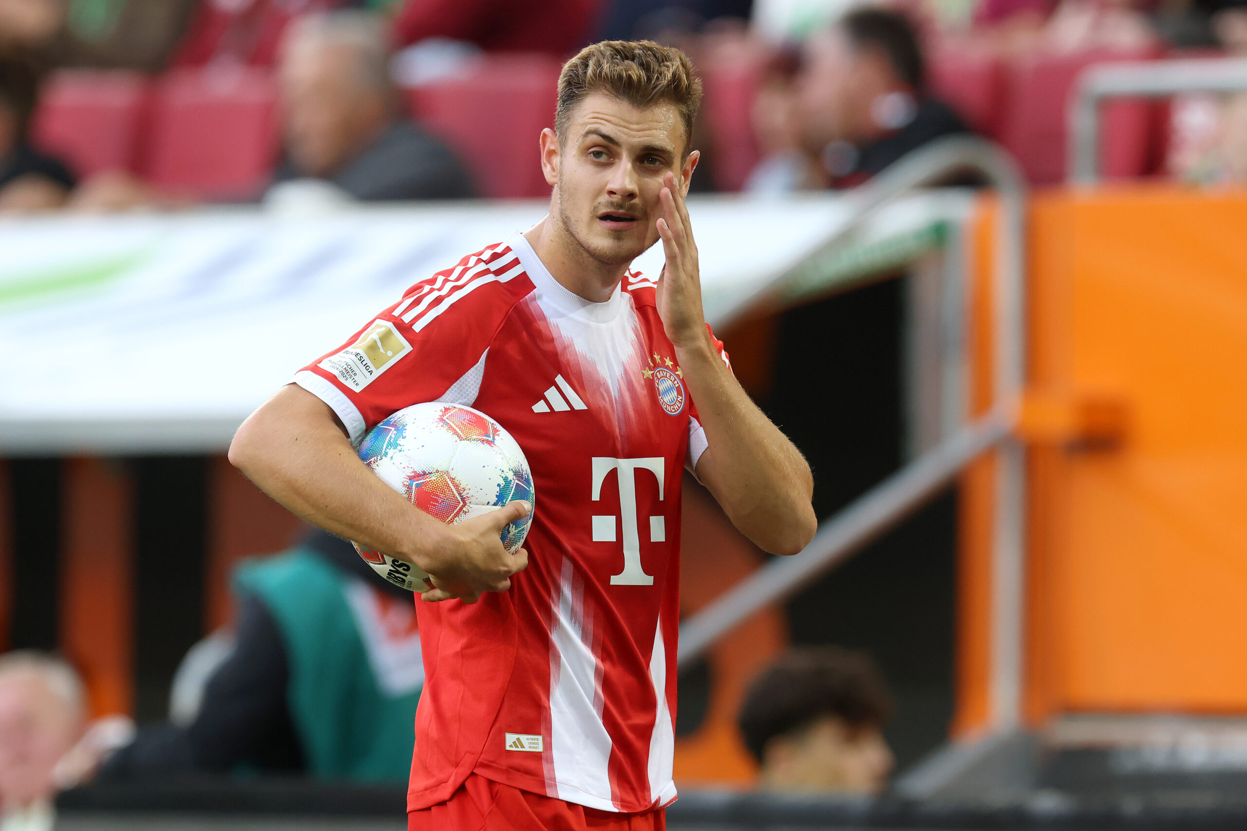 Josip Stanisic fässt sich ins Gesicht. Er hat einen Ball in der Hand und trägt das Trikot des FC Bayern.