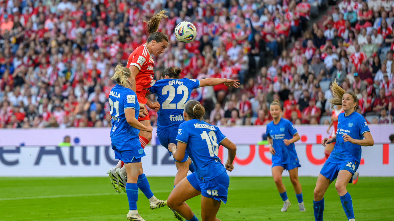Vanessa Gilles steigt für die FC Bayern Frauen in ein Kopfballduell mit Leverkusens Grant. Drumherum mehrere blaue Leverkusen-Spielerinnen.