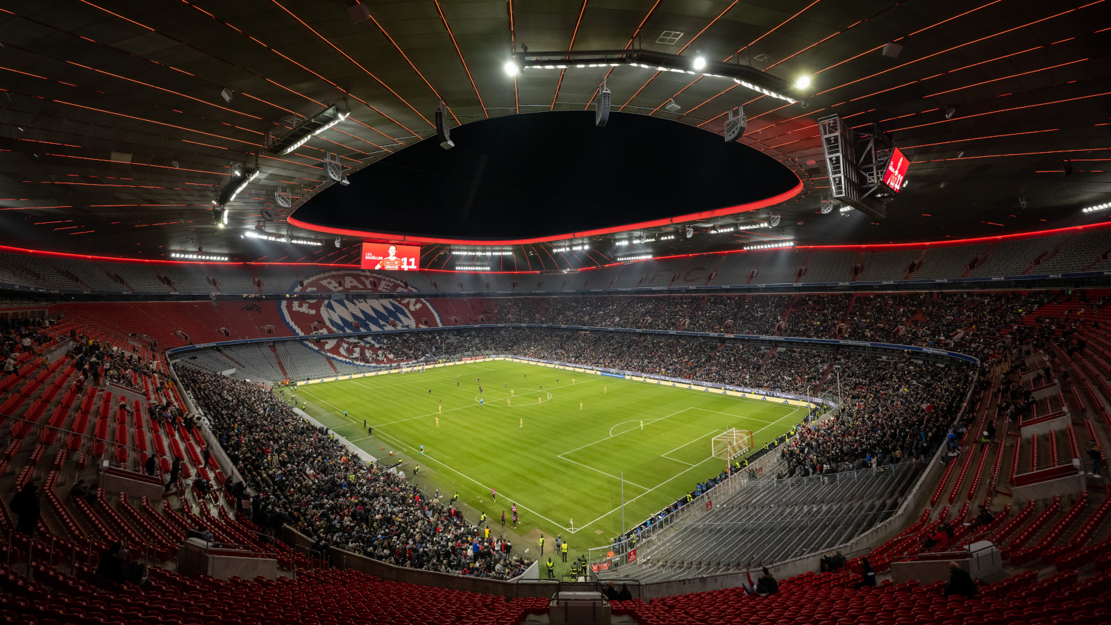 Die Allianz Arena beim Spiel der FC Bayern Frauen gegen den FC Barcelona. Die unteren Ränge sind teilweise gefüllt, nahezu das ganze Stadion ist zu sehen, der Himmel ist dunkel.
