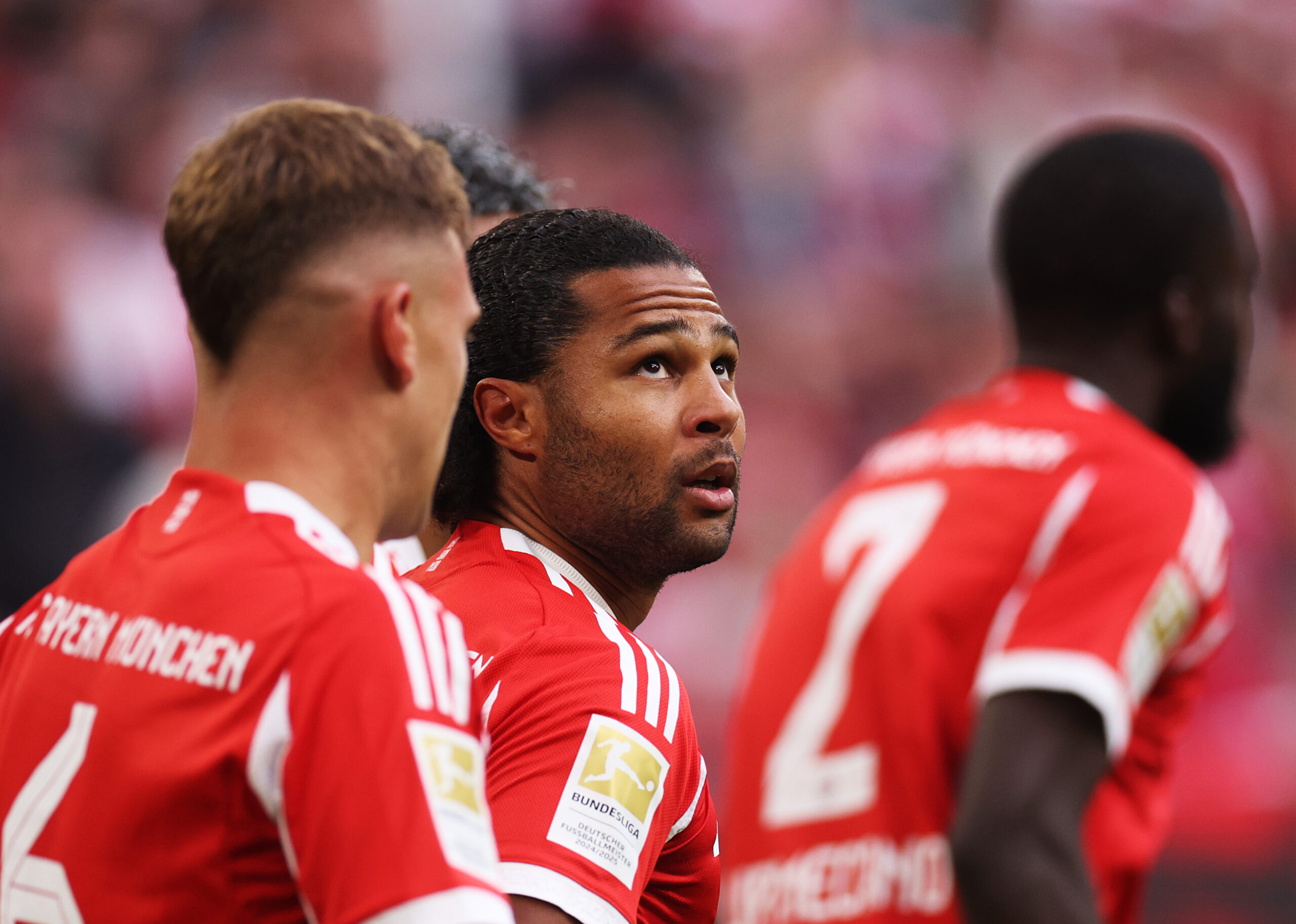 Serge Gnabry im roten Trikot des FC Bayern München. Er schaut nach oben, um ihn herum laufen Kimmich und Upamecano