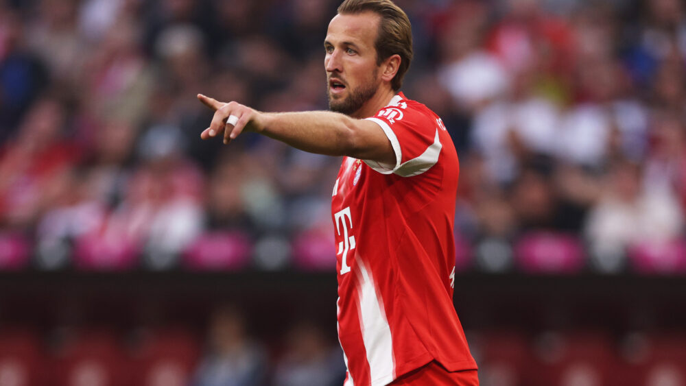 Harry Kane im roten Trikot des FC Bayern. Der Engländer zeigt nach vorn.