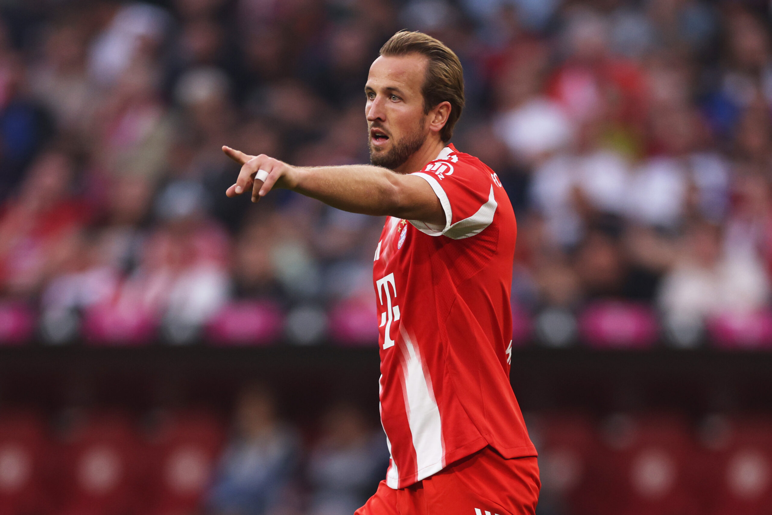 Harry Kane im roten Trikot des FC Bayern. Der Engländer zeigt nach vorn.