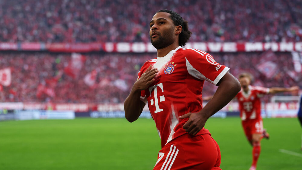 Serge Gnabry jubelt gegen den Hamburger SV und klopft sich auf die Brust. Er trägt das rot-weiße Heimtrikot des FC Bayern München.
