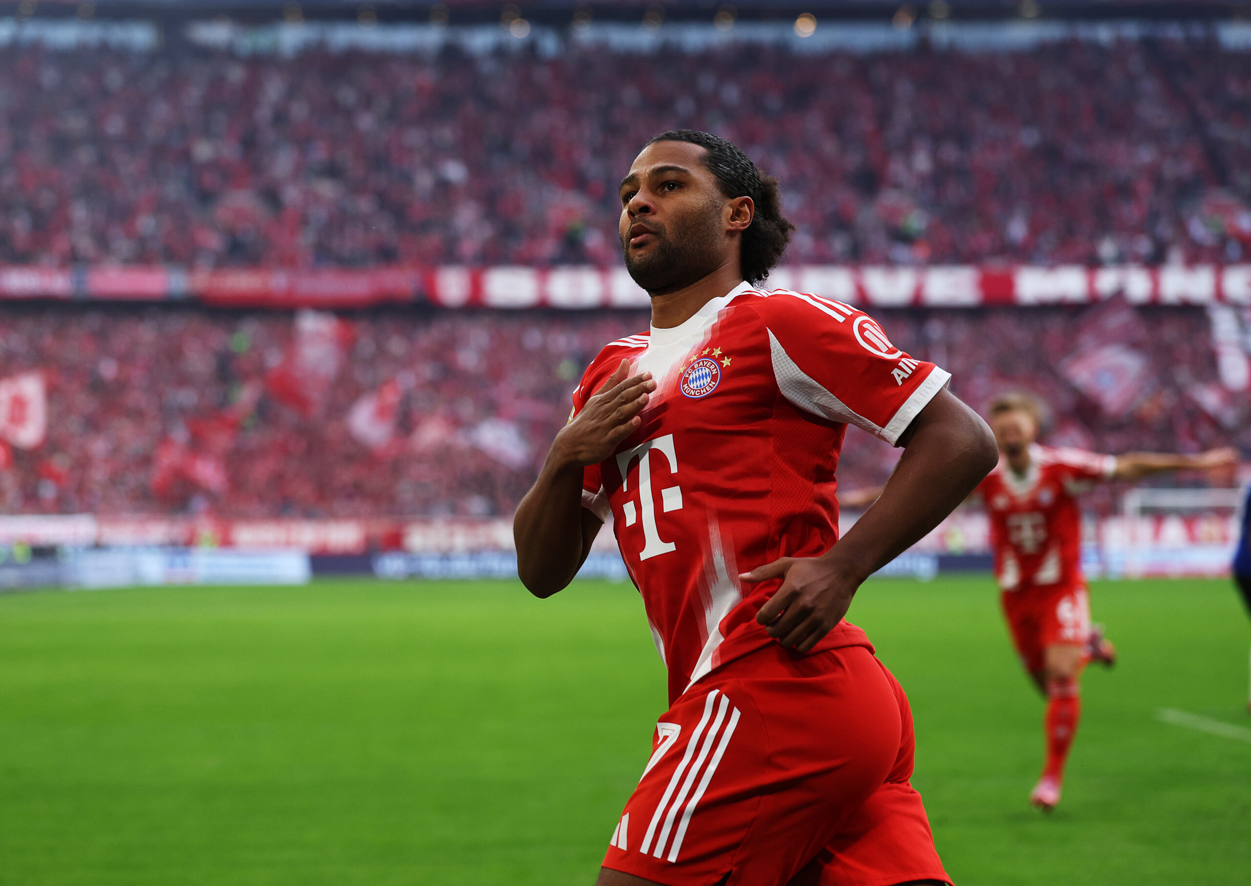 Serge Gnabry jubelt gegen den Hamburger SV und klopft sich auf die Brust. Er trägt das rot-weiße Heimtrikot des FC Bayern München.