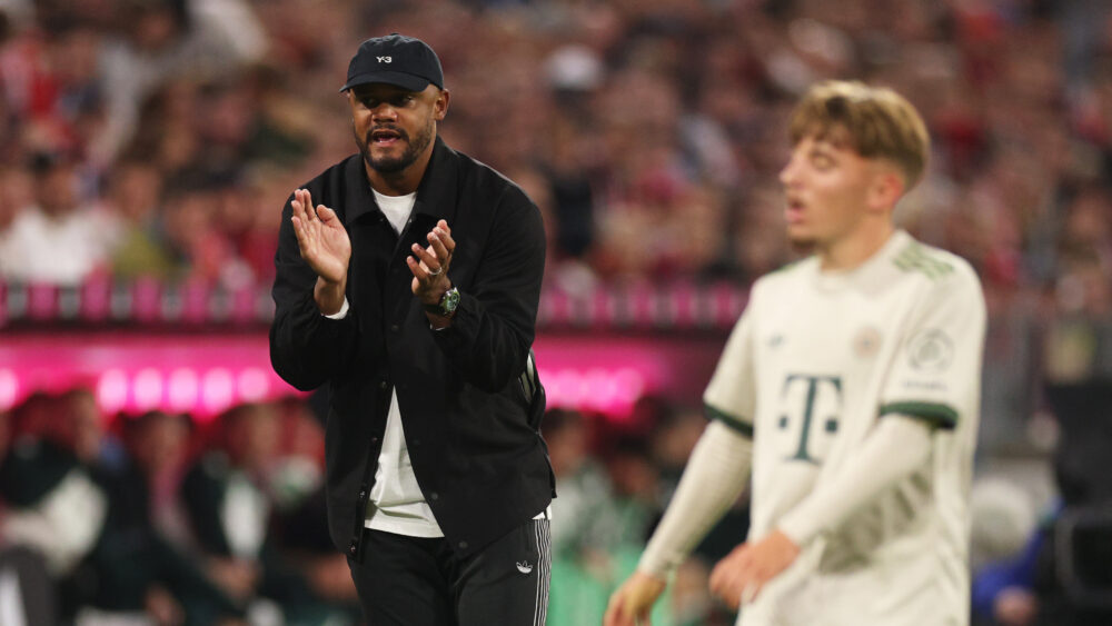 Vincent Kompany klatscht in die Hände, vor ihm ist verschwommen Lennart Karl im Trikot des FC Bayern München zu sehen.