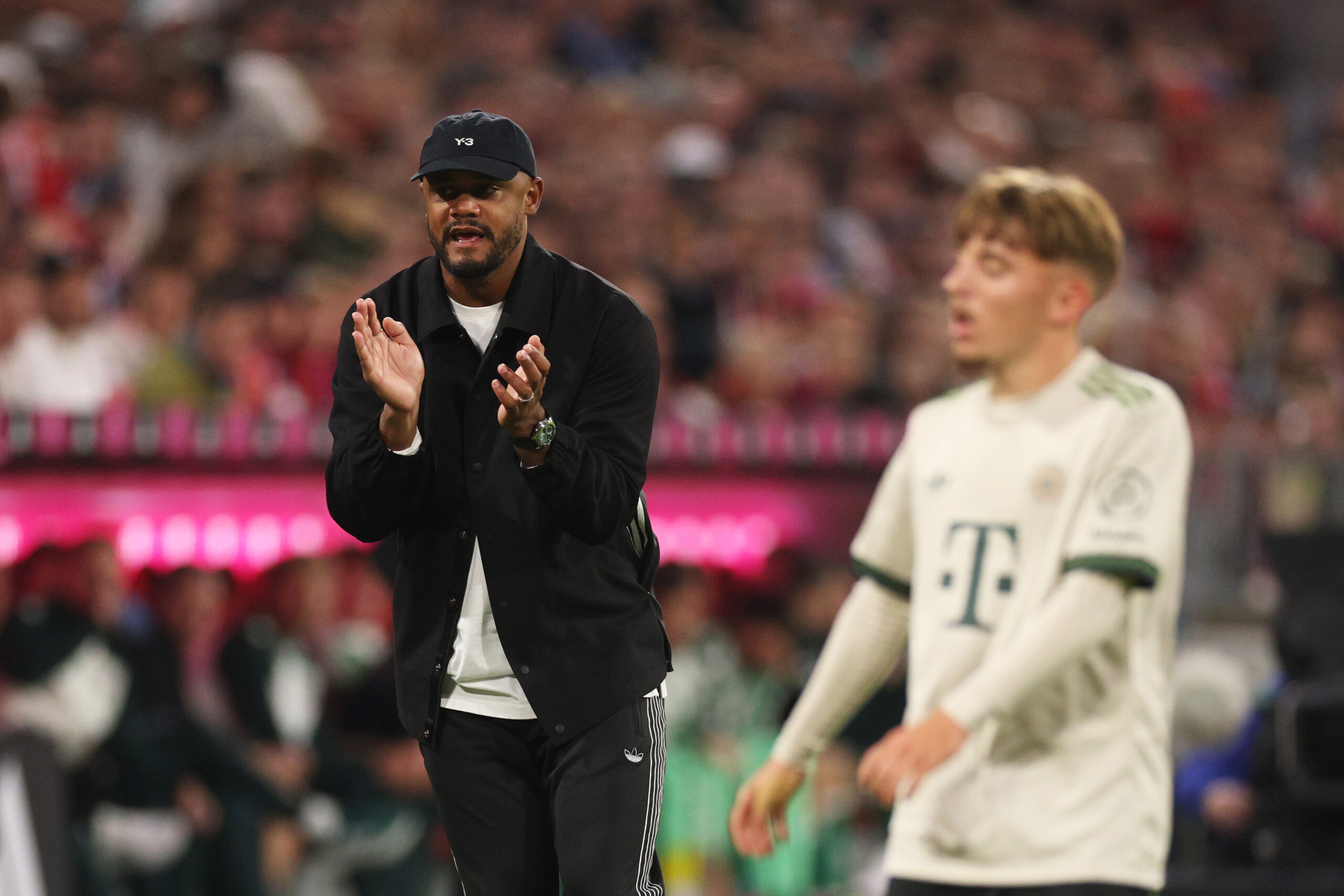 Vincent Kompany klatscht in die Hände, vor ihm ist verschwommen Lennart Karl im Trikot des FC Bayern München zu sehen.