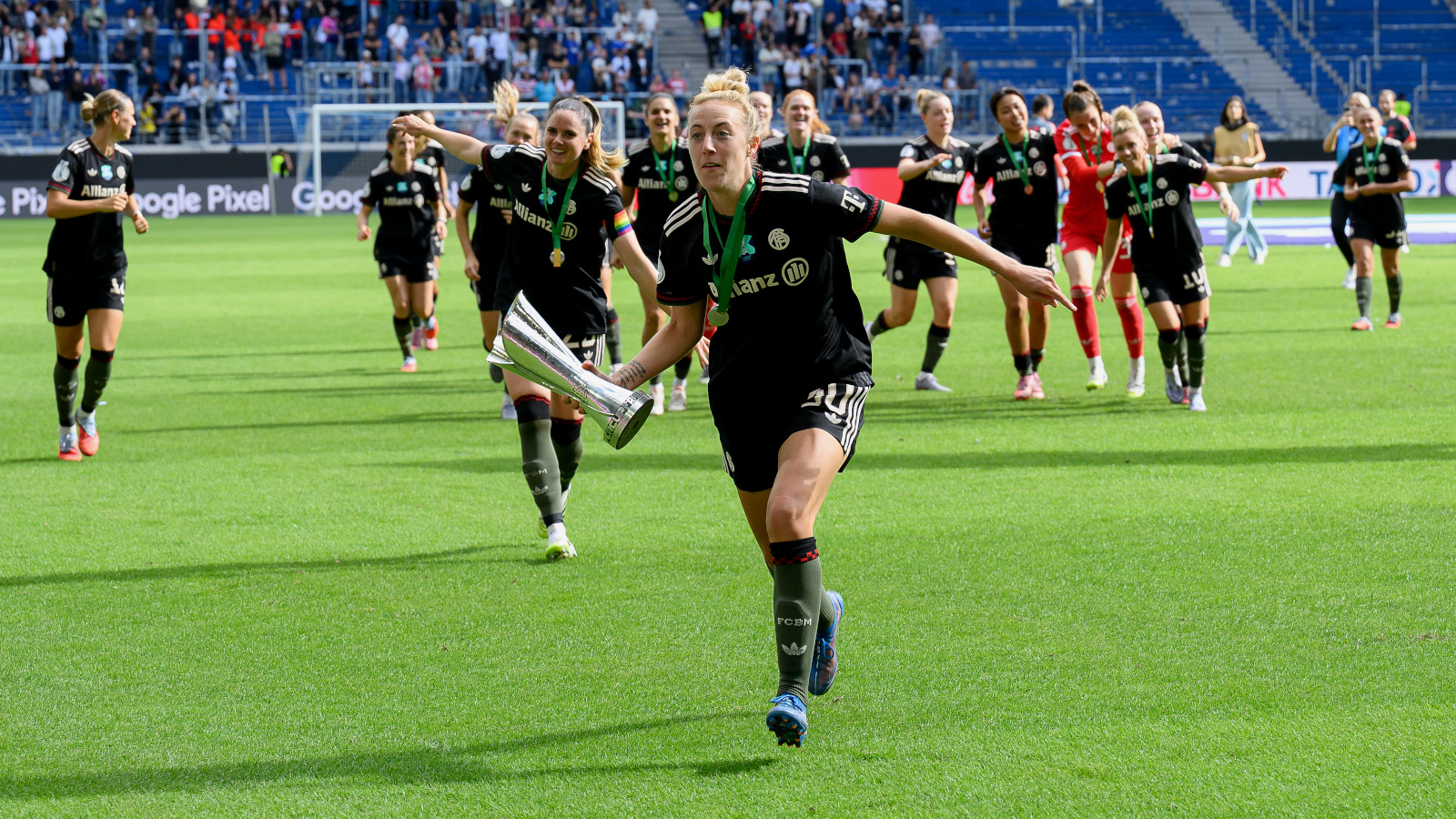 Carolin Simon jubelt im schwarzen Trikot des FC Bayern mit dem Supercup in der Hand. Im Hintergrund jubeln ihre Mitspielerinnen.