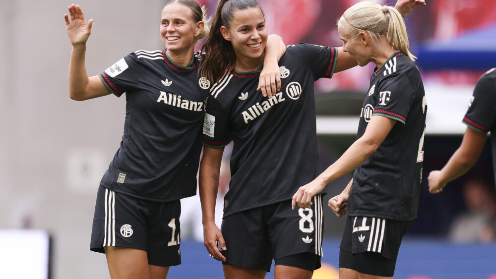 Klara Bühl, Lena Oberdorf und Pernille Harder im dunklen Auswärtstrikot der FC Bayern Frauen. Sie lachen und jubeln über ein Tor.
