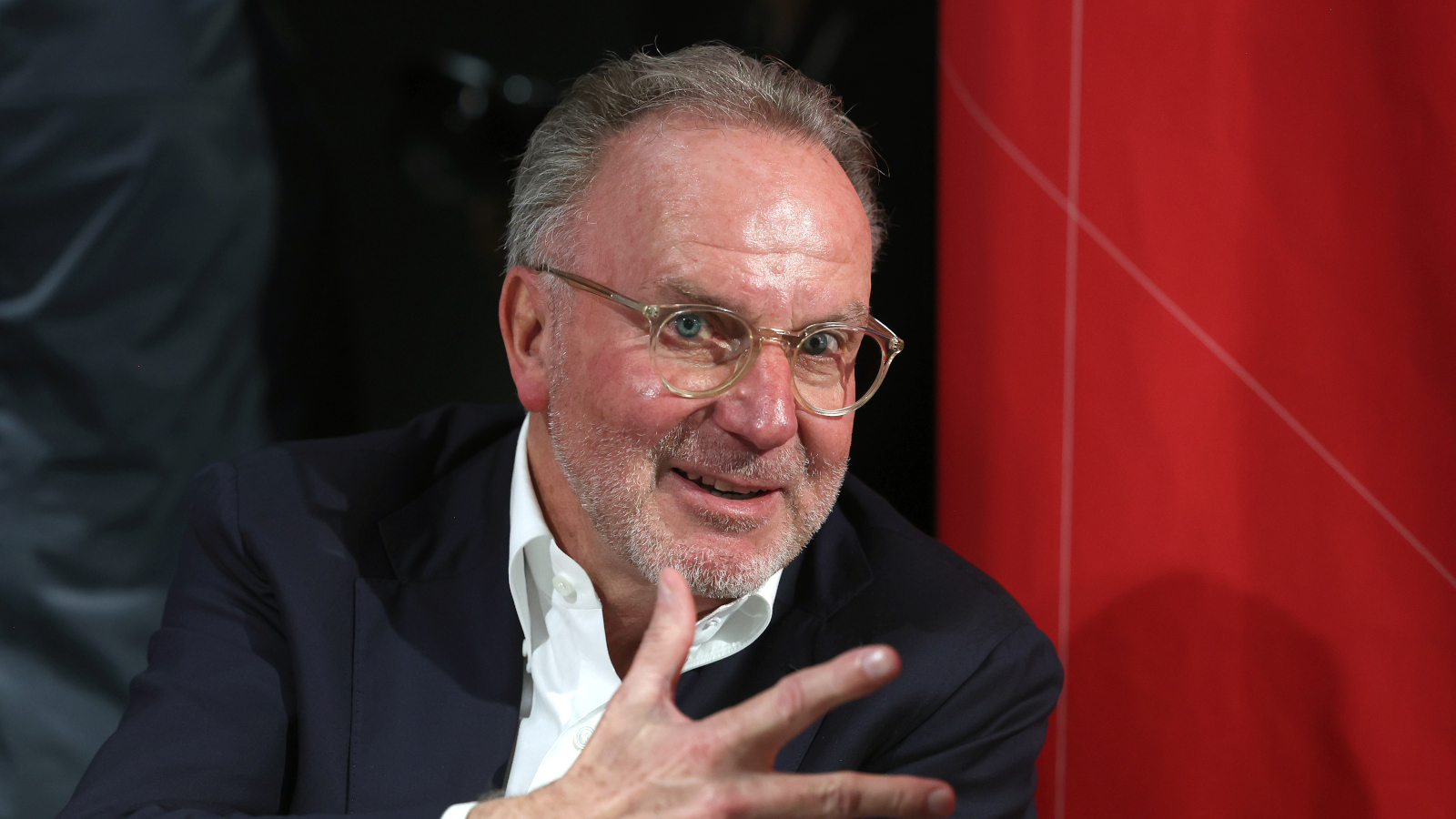 Karl-Heinz Rummenigge (Aufsichtsratsmitglied des FC Bayern) zeigt zwei Finger und den Daumen und lächelt.