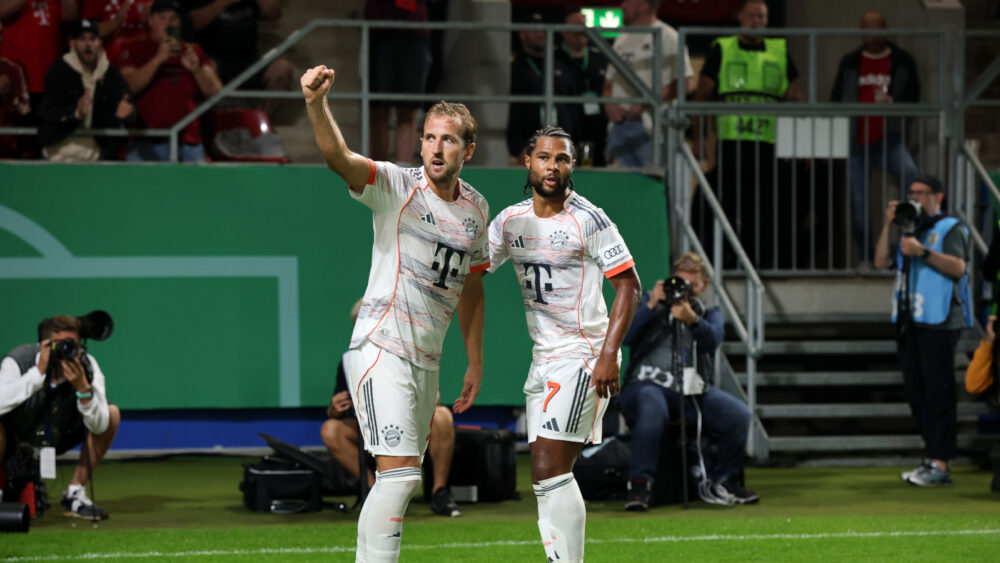 Harry Kane und Serge Gnabry verzaubern die Fans des FC Bayern München. Im Bild sind beide in weißer Spielkleidung zu sehen, Kane hebt die Faust.