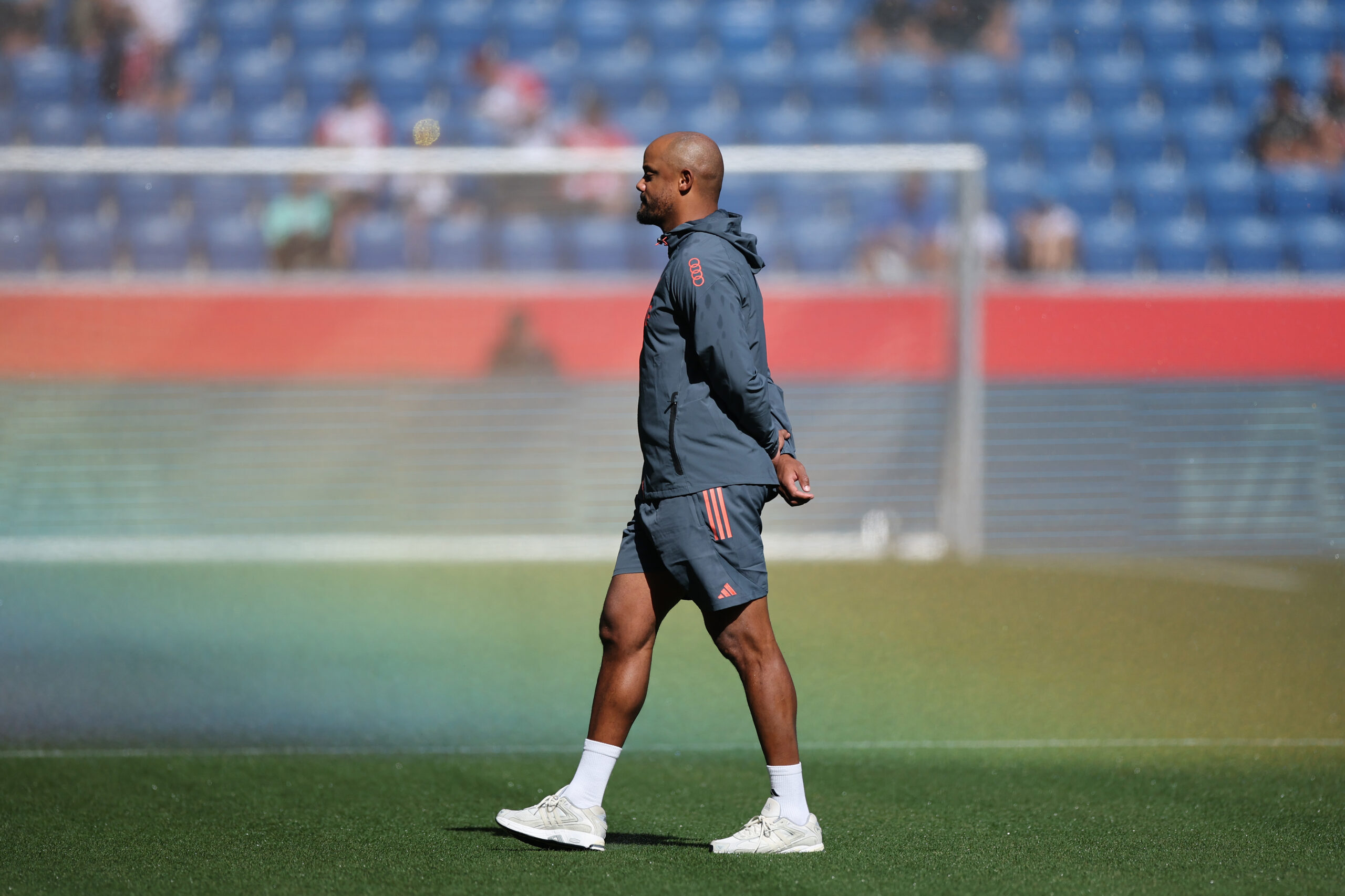 Vincent Kompany läuft über den Rasen. Der Trainer des FC Bayern hat die Arme hinter dem Rücken verschränkt.