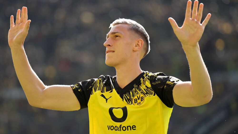 Nico Schlotterbeck vom BVB wird derzeit mit Gerüchten beim FC Bayern ins Gespräch gebracht. Im Bild trägt er ein schwarzgelbes Trikot und hebt beide Arme.