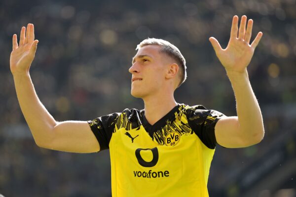 Nico Schlotterbeck vom BVB wird derzeit mit Gerüchten beim FC Bayern ins Gespräch gebracht. Im Bild trägt er ein schwarzgelbes Trikot und hebt beide Arme.
