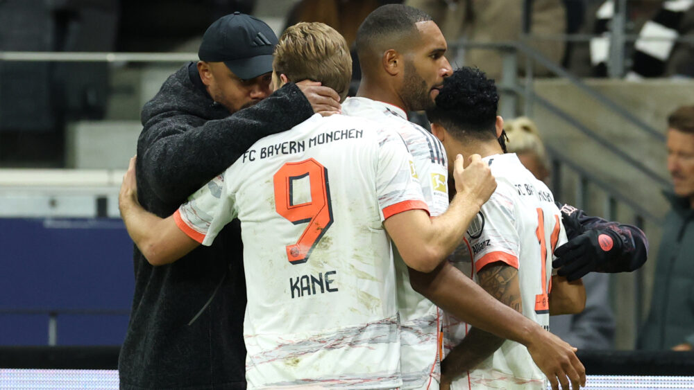 Harry Kane und Vincent Kompany liegen sich in den Armen. Kane trägt das weiße Trikot des FC Bayern.