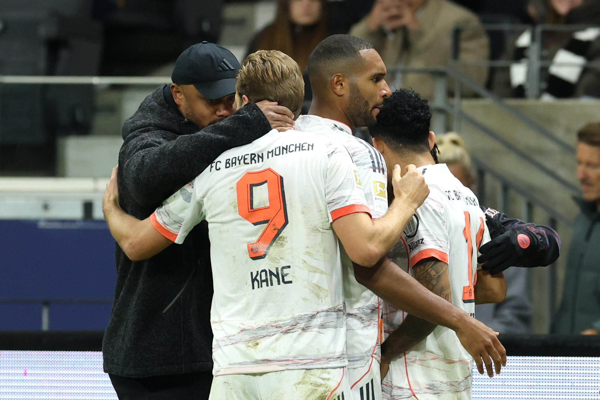 Harry Kane und Vincent Kompany liegen sich in den Armen. Kane trägt das weiße Trikot des FC Bayern.
