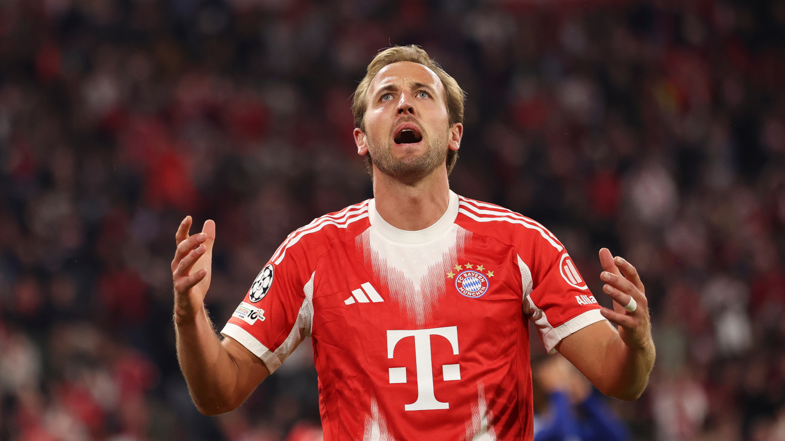 Harry Kane trägt ein rot-weißes Trikot des FC Bayern. Er hadert und hebt die Arme.