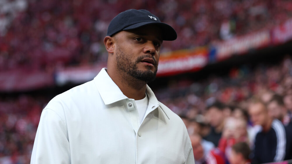 Vincent Kompany im Stadion des FC Bayern München. Er trägt helle Kleidung und eine dunkle Mütze.