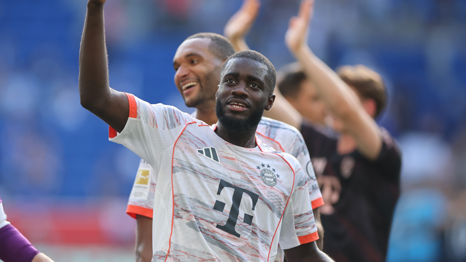 Dayot Upamecano hebt den linken Arm, hinter ihm steht sein Kollege vom FC Bayern München Jonathan Tah und lacht
