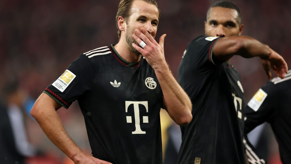 Harry Kane und Jonathan Tah (FC Bayern) halten sich den Arm vors Gesicht.