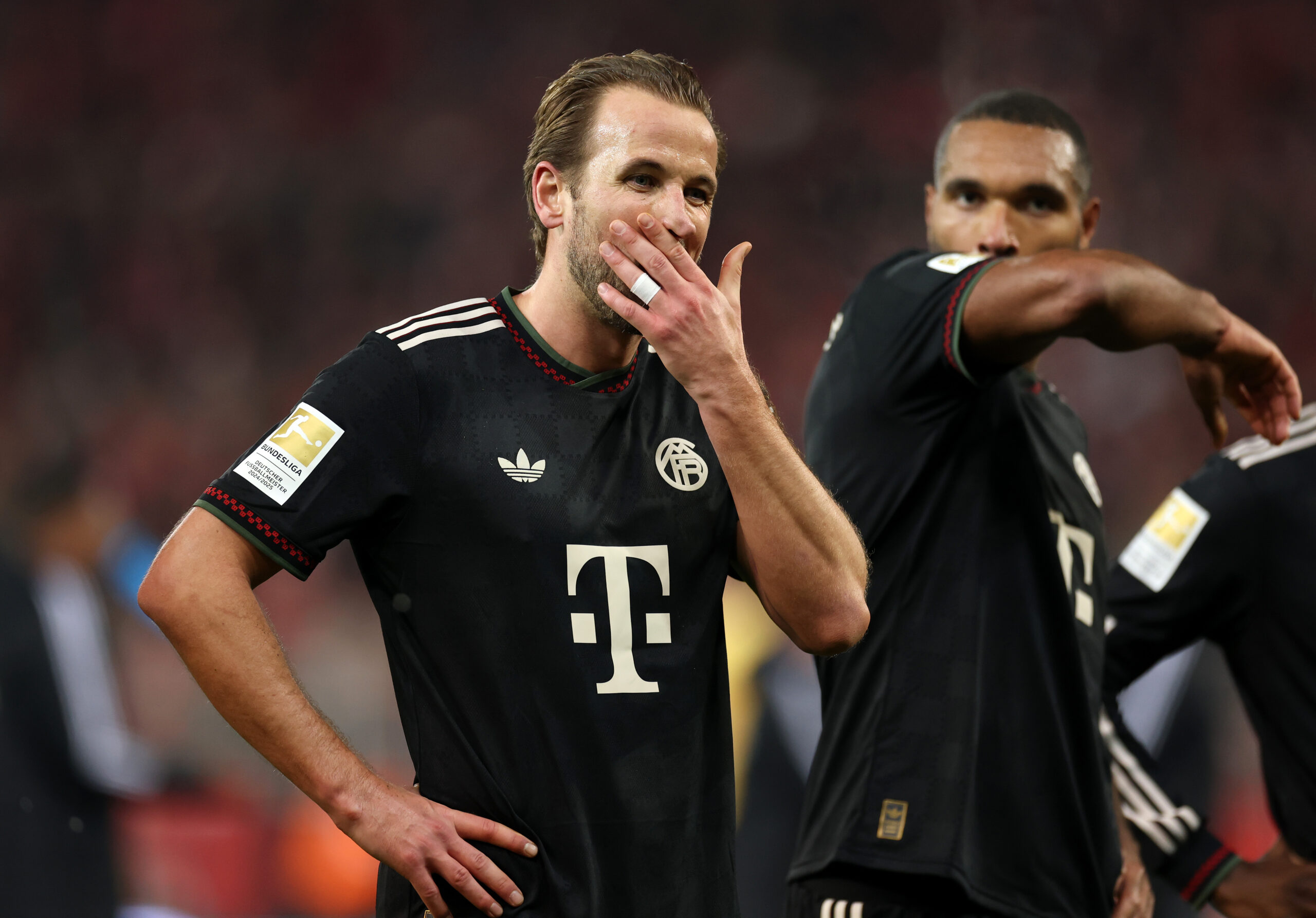 Harry Kane und Jonathan Tah (FC Bayern) halten sich den Arm vors Gesicht.