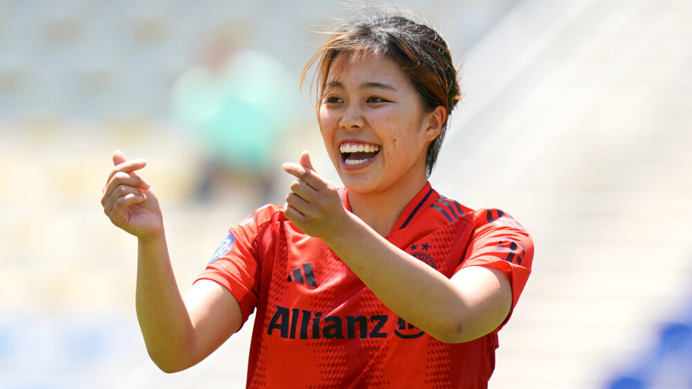 Momoko Tanikawa im Trikot der FC Bayern Frauen. Sie lacht und zeigt mit ihren beiden Händen zwei Herzen, indem sie Finger und Daumen kreuzt.