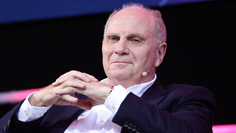 Uli Hoeneß nimmt die Hände vor dem Gesicht zusammen und lächelt zufrieden.