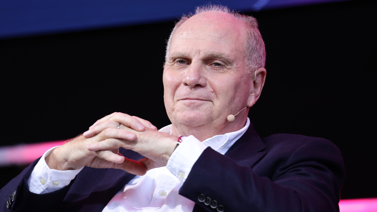 Uli Hoeneß nimmt die Hände vor dem Gesicht zusammen und lächelt zufrieden.