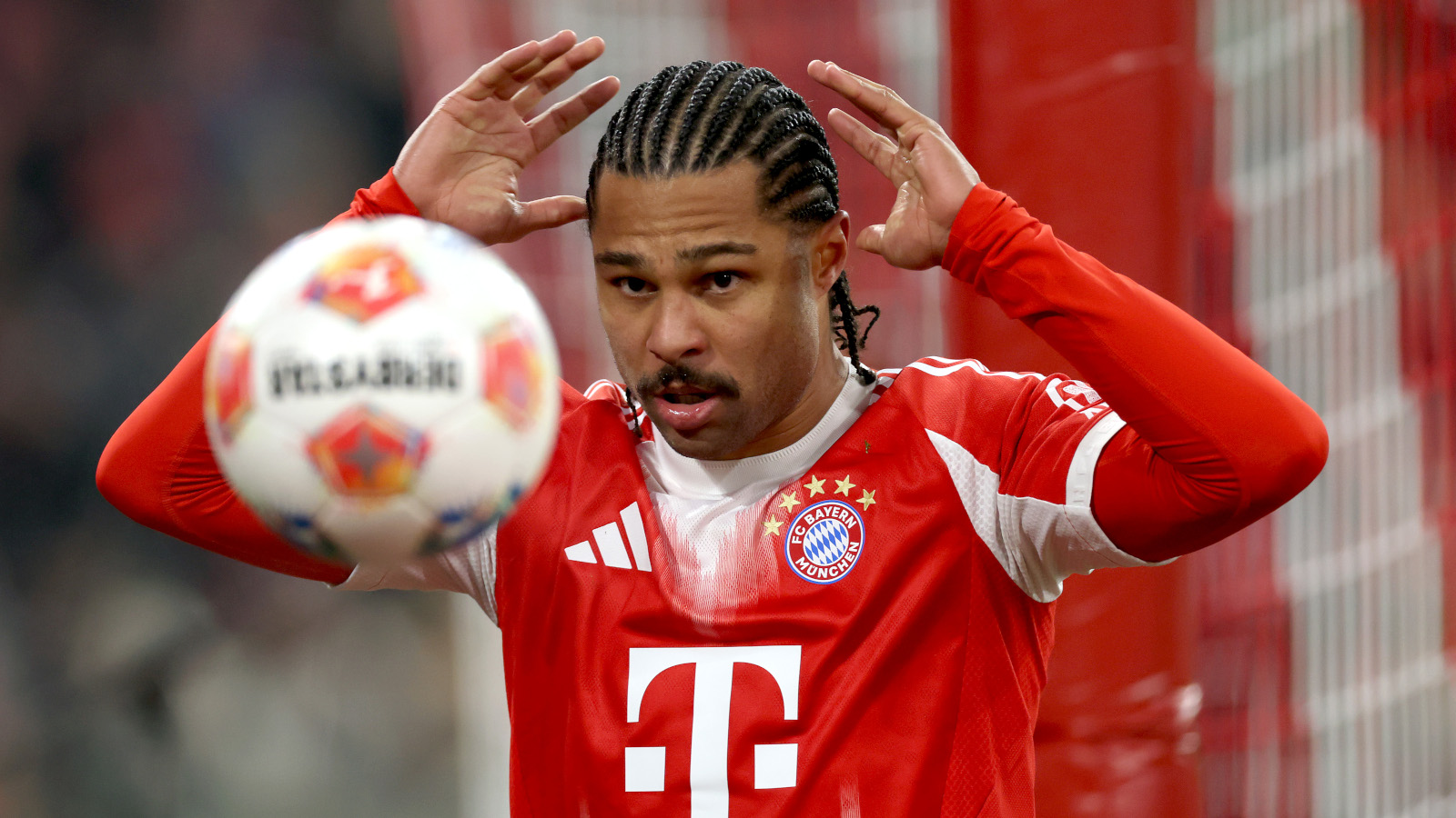 Serge Gnabry hält die Hände über dem Kopf. Er wirft offenbar den Ball, der vor ihm zu sehen ist. Er trägt ein rot-weißes Trikot des FC Bayern.