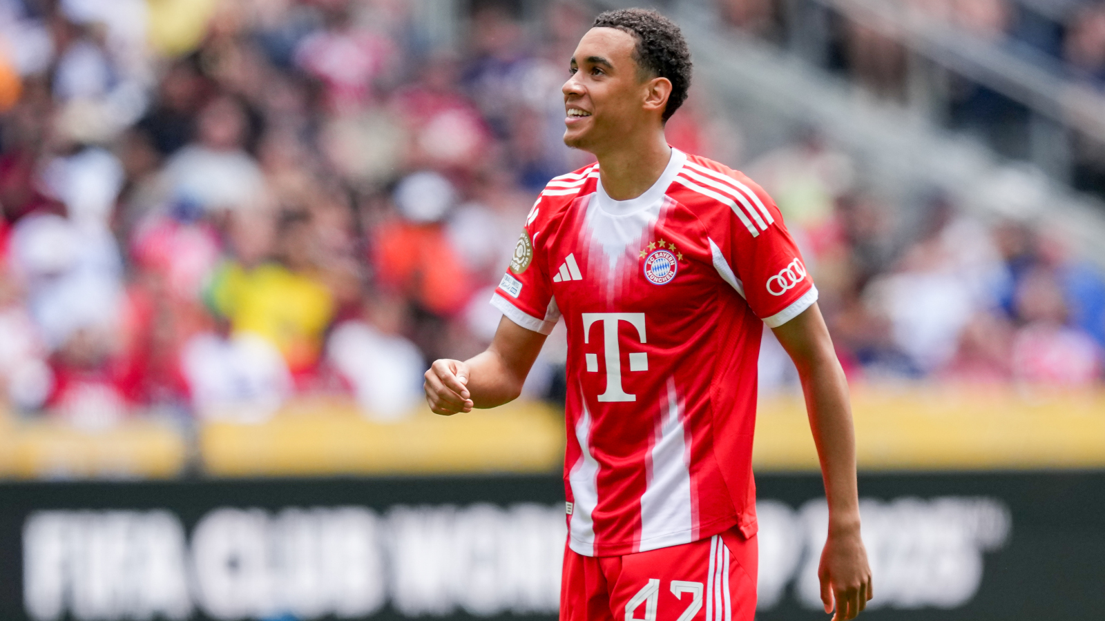 Jamal Musiala im Trikot des FC Bayern. Er schaut leicht nach oben und lächelt.