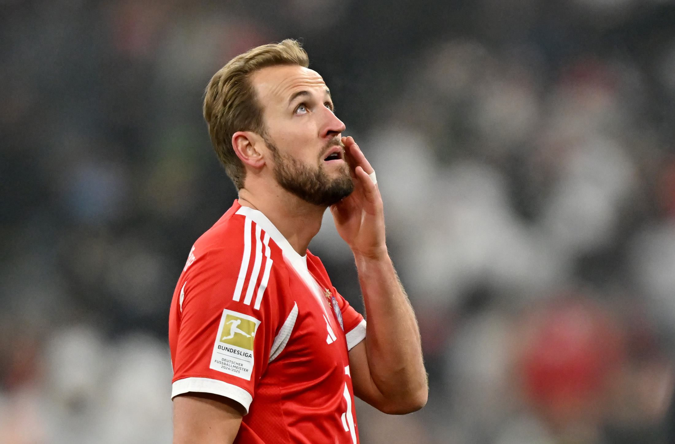 Harry Kane schaut mit finsterem Blick nach oben, runzelt die Stirn und fässt sich ins Gesicht. Er trägt das rot-weiße Trikot des FC Bayern.