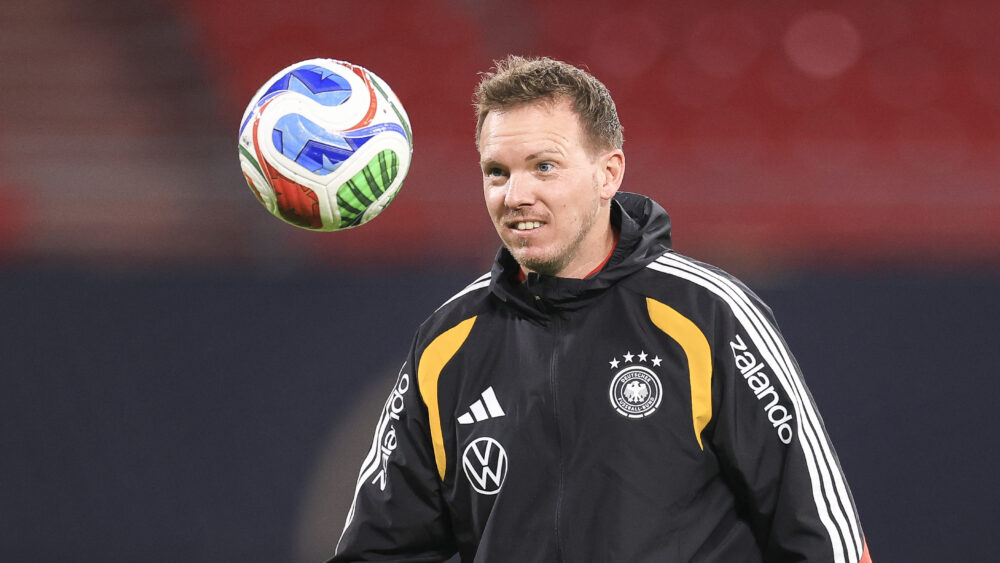 Julian Nagelsmann schaut einem in der Luft fliegenden Ball hinterher und lächelt.