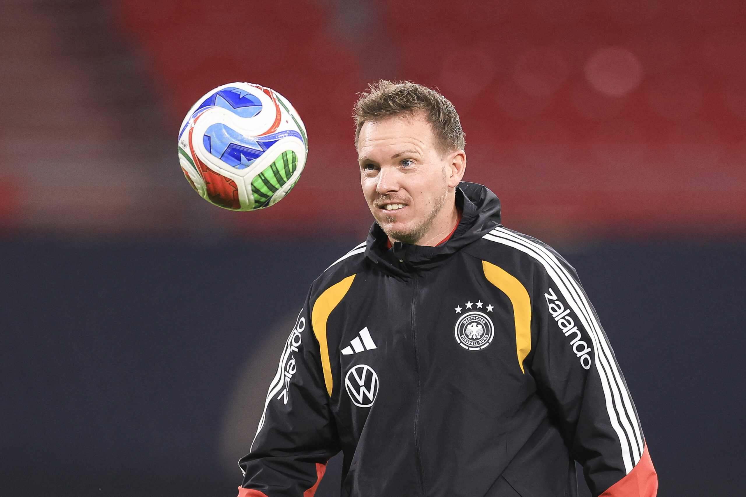 Julian Nagelsmann schaut einem in der Luft fliegenden Ball hinterher und lächelt.