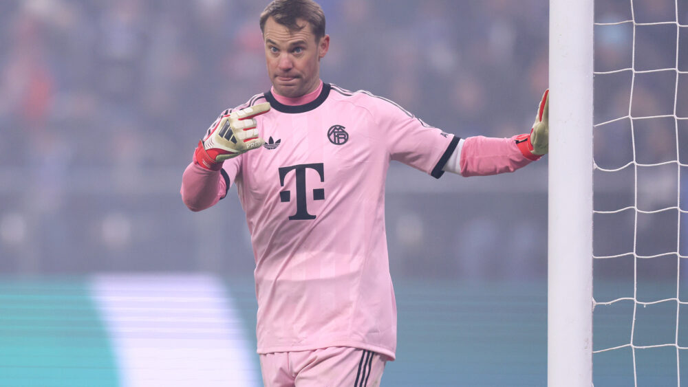Manuel Neuer im rosafarbenen Trikot des FC Bayern. Er zeigt mit dem Finger in Richtung Pfosten.