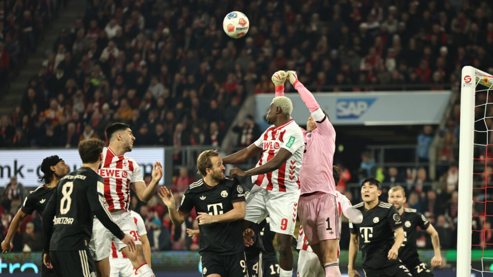 Manuel Neuer (FC Bayern) im Luftduell mit den Spielern des 1. FC Köln. Der Strafraum ist voll mit Spielern beider teams, Neuer springt nach oben und reißt die Fäuste hoch.