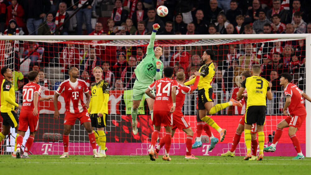 Manuel Neuer springt hoch und faustet den Ball. Um ihn herum stehen Spieler des FC Bayern und des BVB.