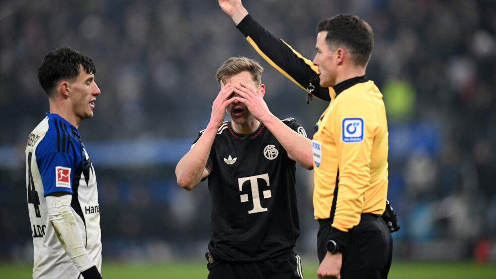 Harm Osmers zeigt eine Gelbe Karte, Joshua Kimmich vom FC Bayern schlägt die Hände vor dem Gesicht zusammen.