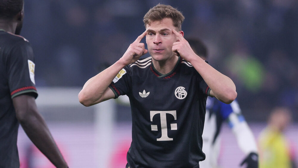 Joshua Kimmich im dunklen Auswärtstrikot des FC Bayern. Er zeigt sich mit beiden Fingern an die Stirn.