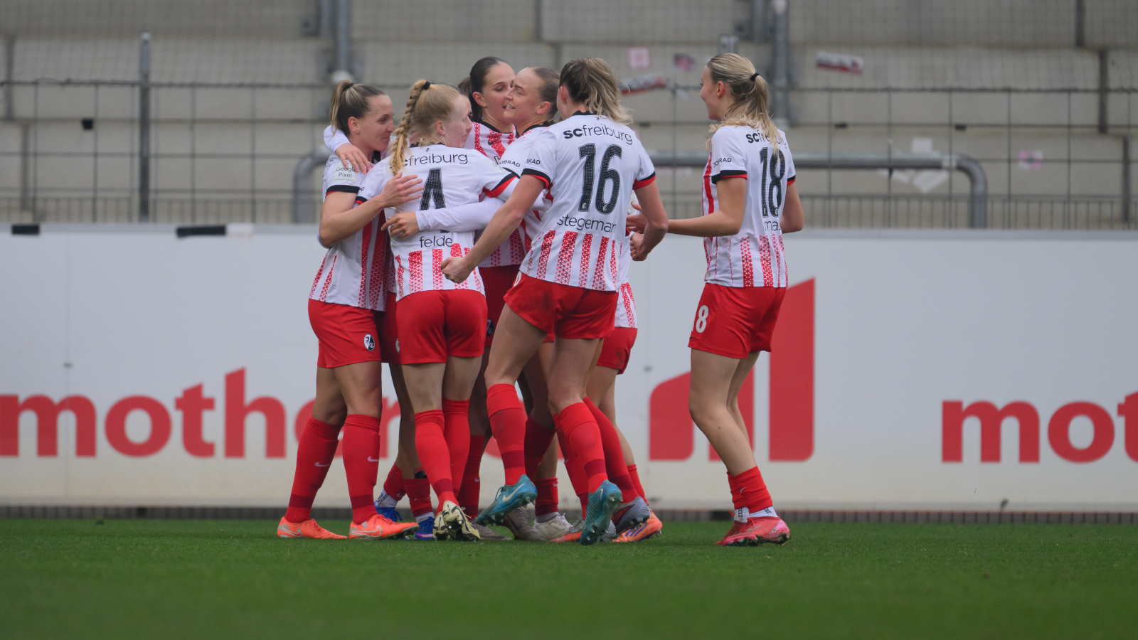 der SC Freiburg jubelt in seinen weißen Auswärtstrikots mit roten Hosen und roten Streifen. Im Hintergrund ist eine Werbebande und eine leere Tribüne zu sehen. Treffen sie auch gegen die FC Bayern Frauen?