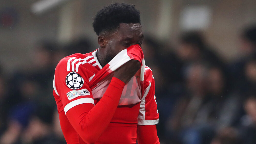 Alphonso Davies zieht sich das rot-weiße Trikot des FC Bayern übers halbe Gesicht.