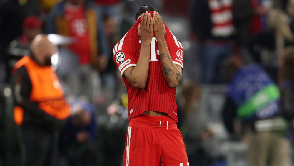 Michael Olise zieht sich das Trikot des FC Bayern über sein Gesicht.