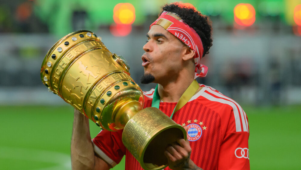 Luis Díaz jubelt im rot-weißen Trikot des FC Bayern, er hat ein Tuch um den Kopf gewickelt und hält den DFB-Pokal in beiden Händen.